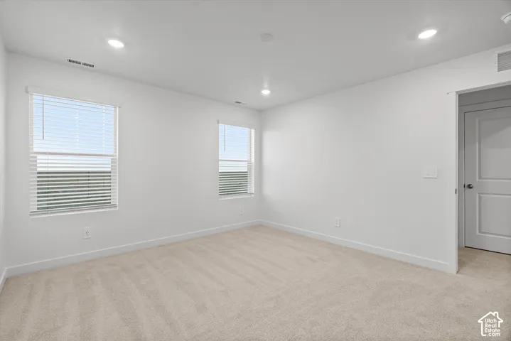 Neutral-toned wall-to-wall carpeting, recessed LED lighting, dual windows with fitted blinds, and a solid-core interior door