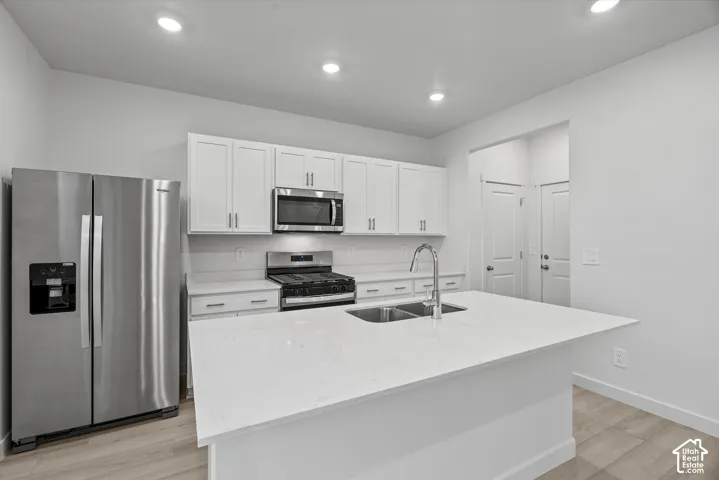 Kitchen featuring white cabinetry, stone-surface island countertop with a double-basin undermount sink, stainless steel appliances, and wood-finish flooring