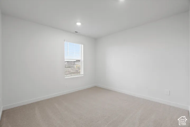 Neutral interior room featuring neutral-toned carpeting, recessed ceiling lighting, and a single window with fitted blinds