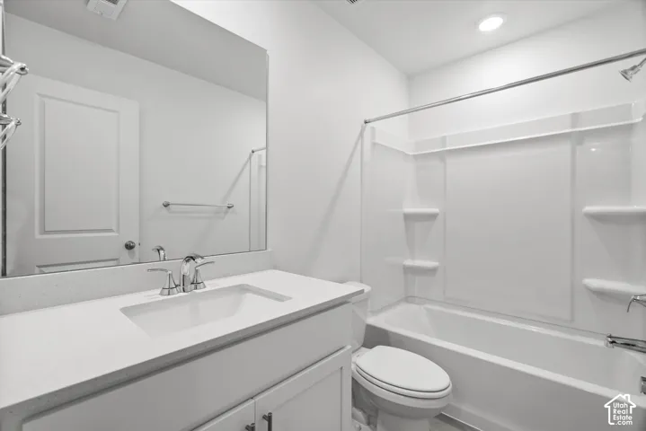 Bathroom featuring a white vanity with a solid-surface countertop, rectangular undermount sink, expansive wall-mounted mirror, and a tub-shower combination with integrated shelving