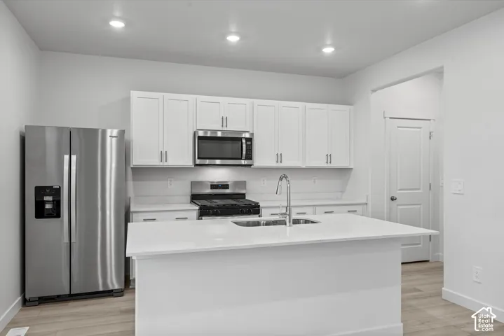 Kitchen featuring white shaker-style cabinetry, quartz countertops, a central island with an undermount sink, stainless steel appliances, and wood-finish flooring