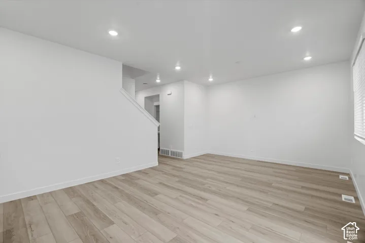 Open interior space featuring light wood-finish flooring, neutral walls, recessed lighting, and horizontal blinds