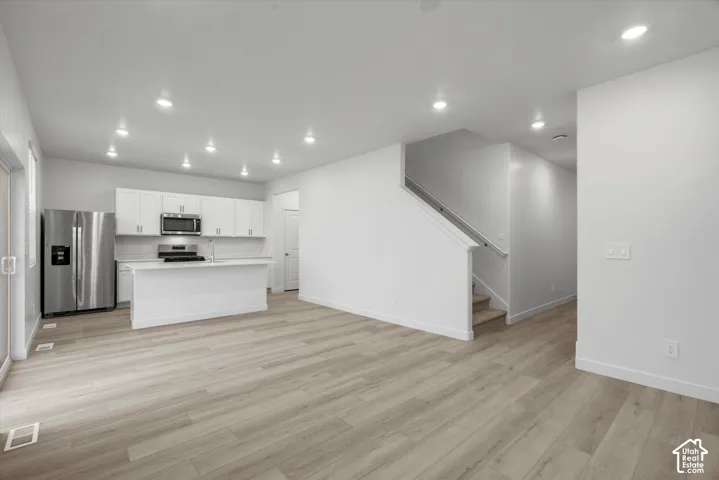 Kitchen featuring white cabinetry, an island, and stainless steel appliances, complemented by wood-finish flooring and recessed lighting
