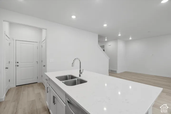 Kitchen island featuring a quartz countertop, under-mount dual-basin stainless steel sink, gooseneck faucet, and white shaker-style cabinetry, complemented by wood-finish flooring and recessed lighting