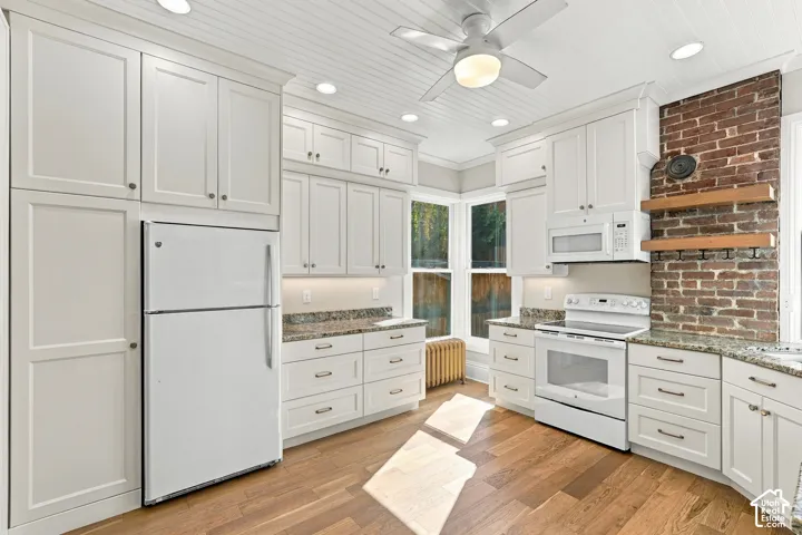 Beautifully renovated kitchen with white cabinetry, granite countertops, oak flooring, and original exposed brick.