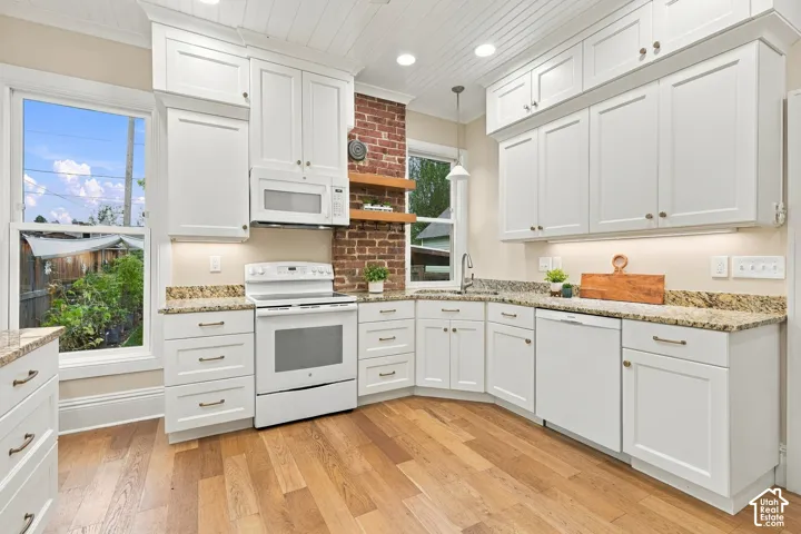 Beautifully renovated kitchen with white cabinetry, granite countertops, oak flooring, and original exposed brick.