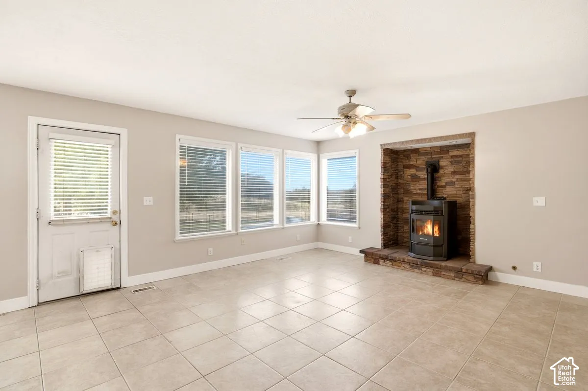 Neutral-toned tile flooring, multiple windows, built-in stone-surround hearth, and ceiling-mounted light fixture with fan