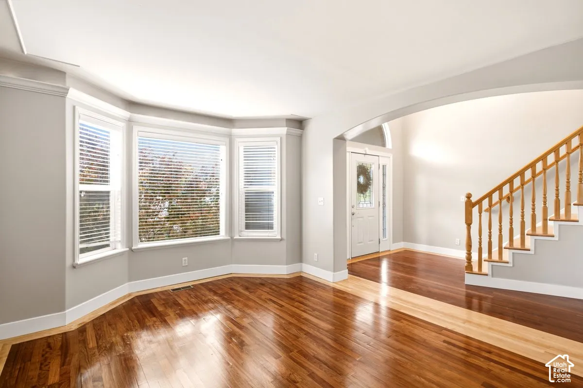 Wood-finish flooring, bay window, arched entryway, and staircase with wooden handrail