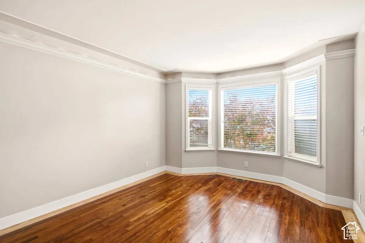 Interior room featuring wood-finish flooring, a three-panel bay window, crown molding, and neutral wall paint