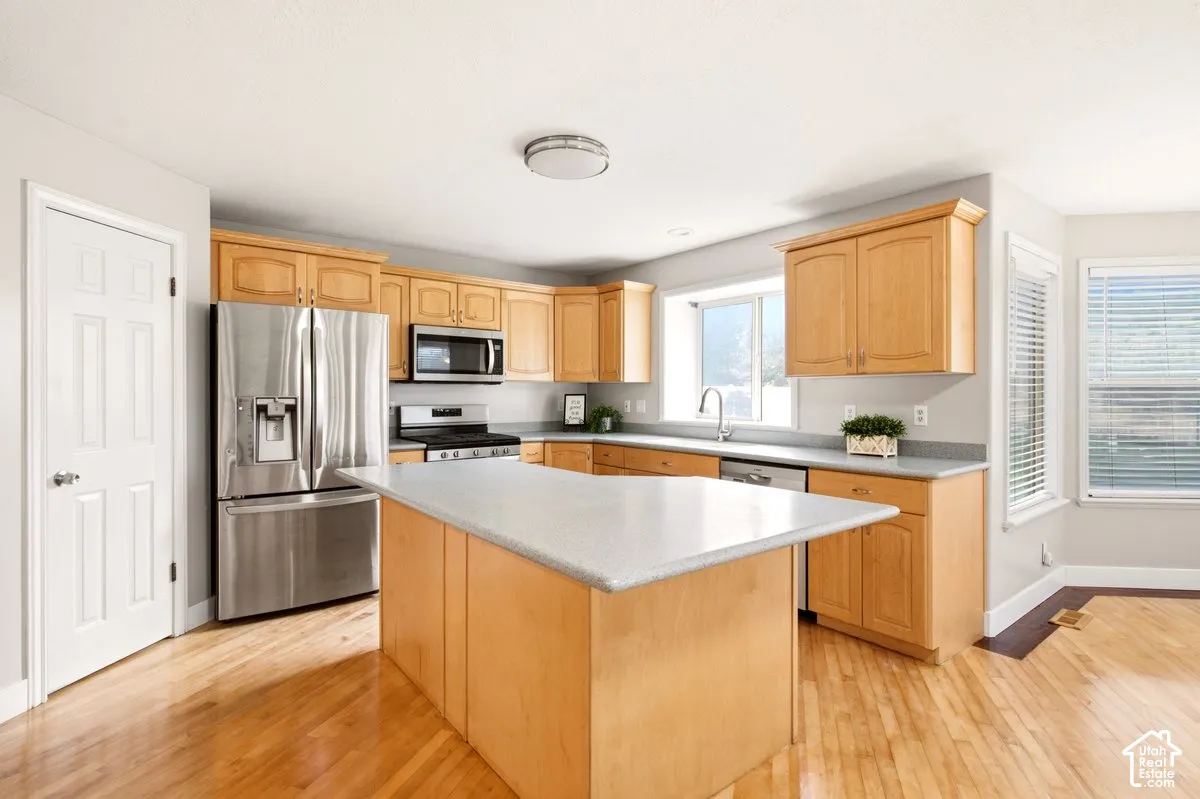 Kitchen featuring natural wood cabinetry, central island, stainless steel appliances, solid-surface countertops, and wood-finish flooring