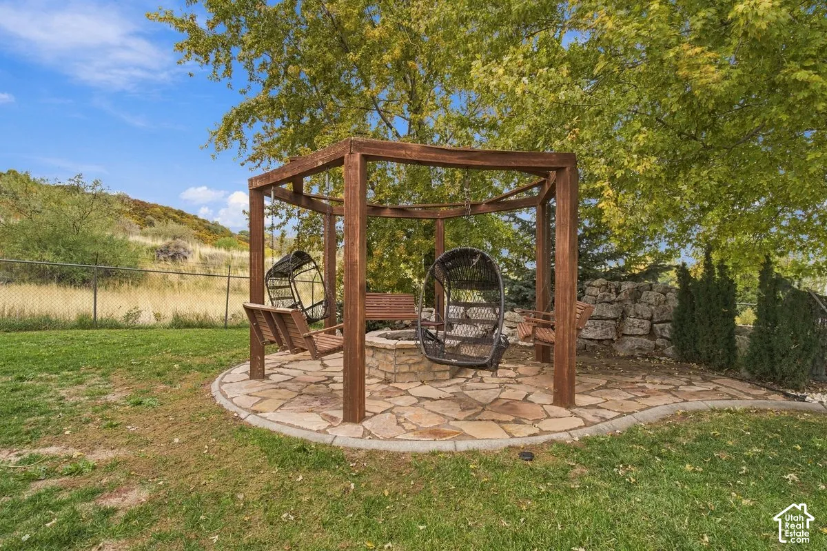 Outdoor space featuring a timber-frame pergola, stone-paved patio, custom stone fire pit, and tiered rock retaining wall