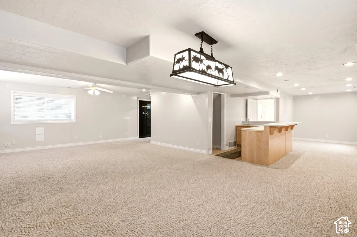 Open-concept space featuring wall-to-wall carpeting, a built-in wet bar with light-wood cabinetry, a decorative rectangular chandelier, and a secured safe room door
