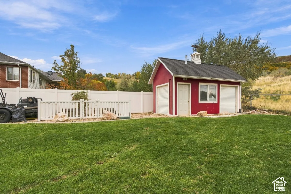 Detached outbuilding featuring a red exterior, white trim, dual roll-up doors, a single entry door, and a cupola, situated on a lot with a white vinyl fence and manicured lawn