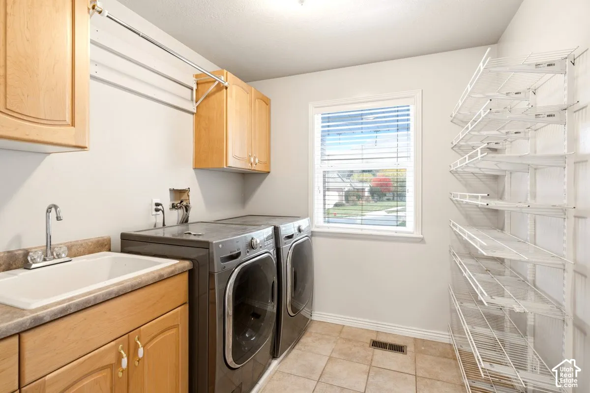Laundry area featuring light wood-finish cabinetry, a utility sink with a stone-finish countertop, wall-mounted metal shelving, and ceramic tile flooring