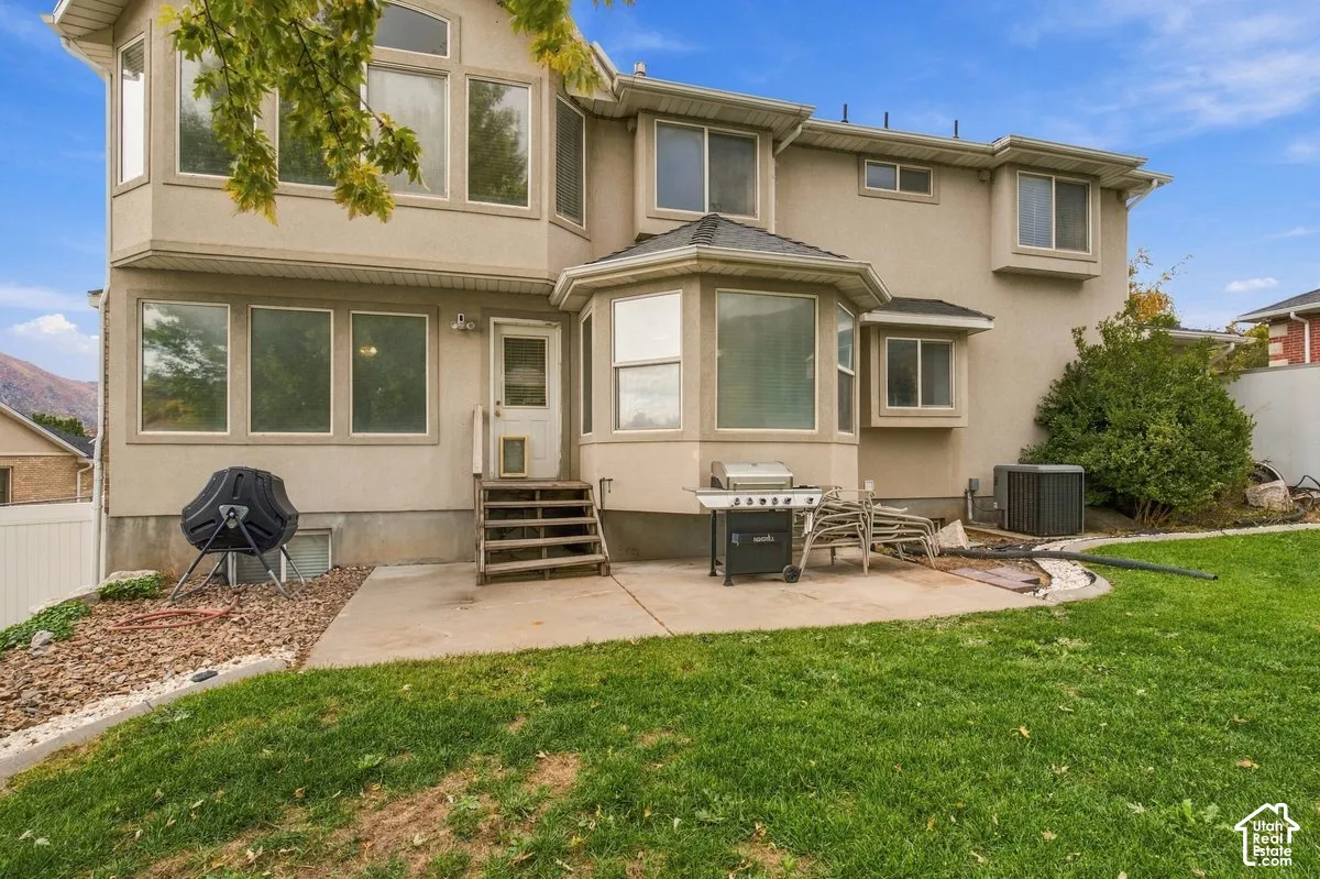 Two-story stucco exterior featuring multi-pane windows, a concrete rear patio, and a grass lawn