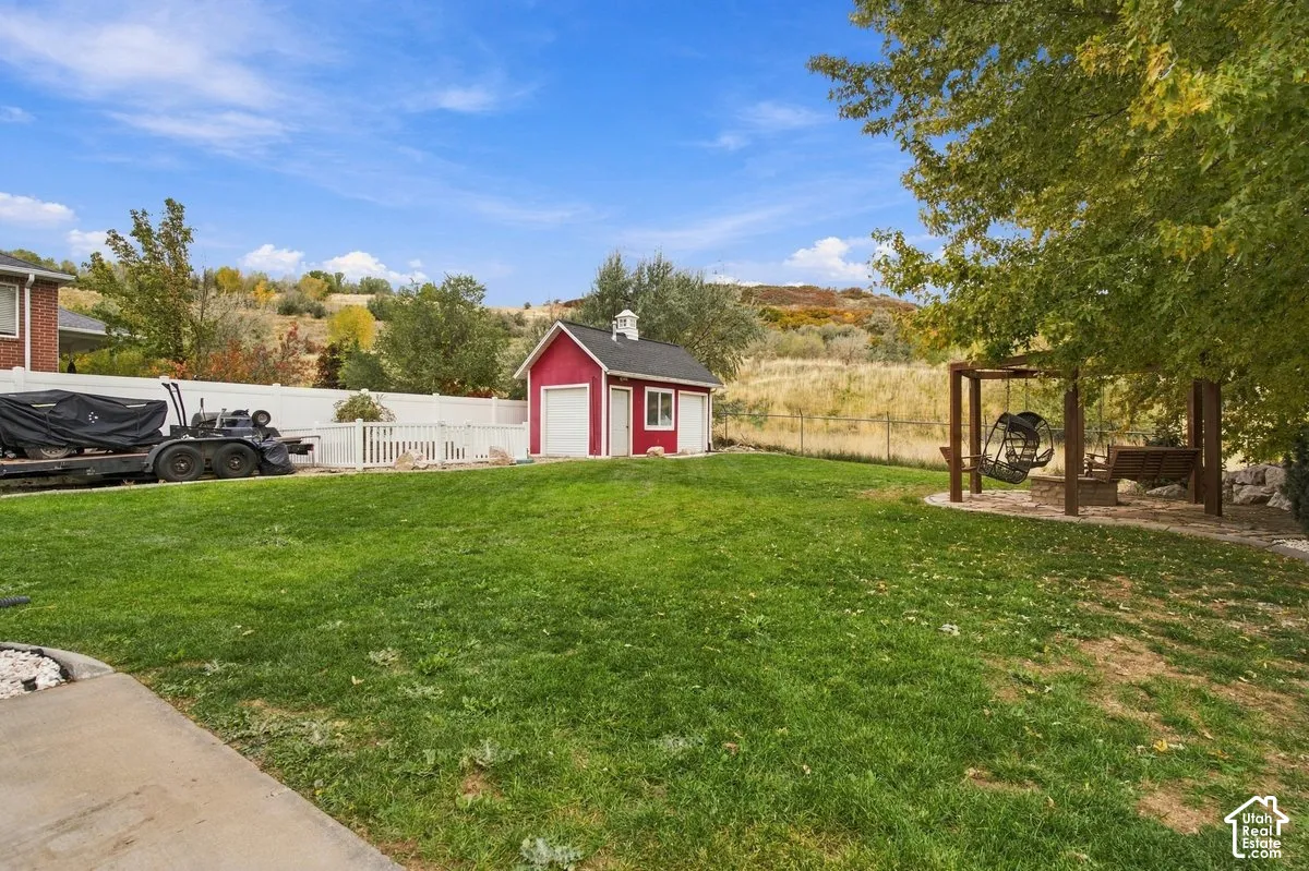 Expansive backyard featuring a manicured lawn, detached barn-style structure, wood pergola, and white vinyl privacy fencing