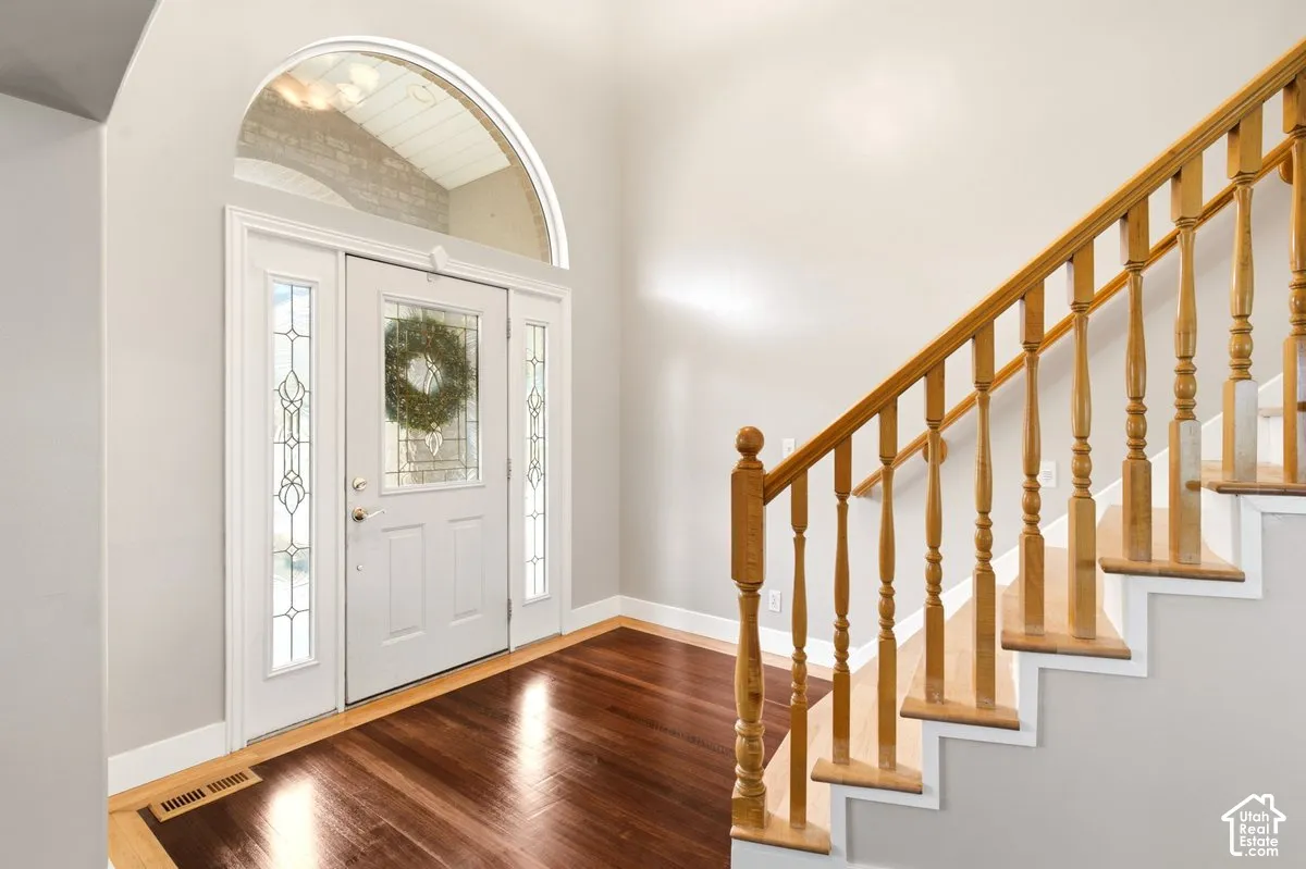 Entryway featuring high ceilings, wood-finish flooring, an arched transom window, a white entry door with glass paneling, and a wood staircase with decorative balusters
