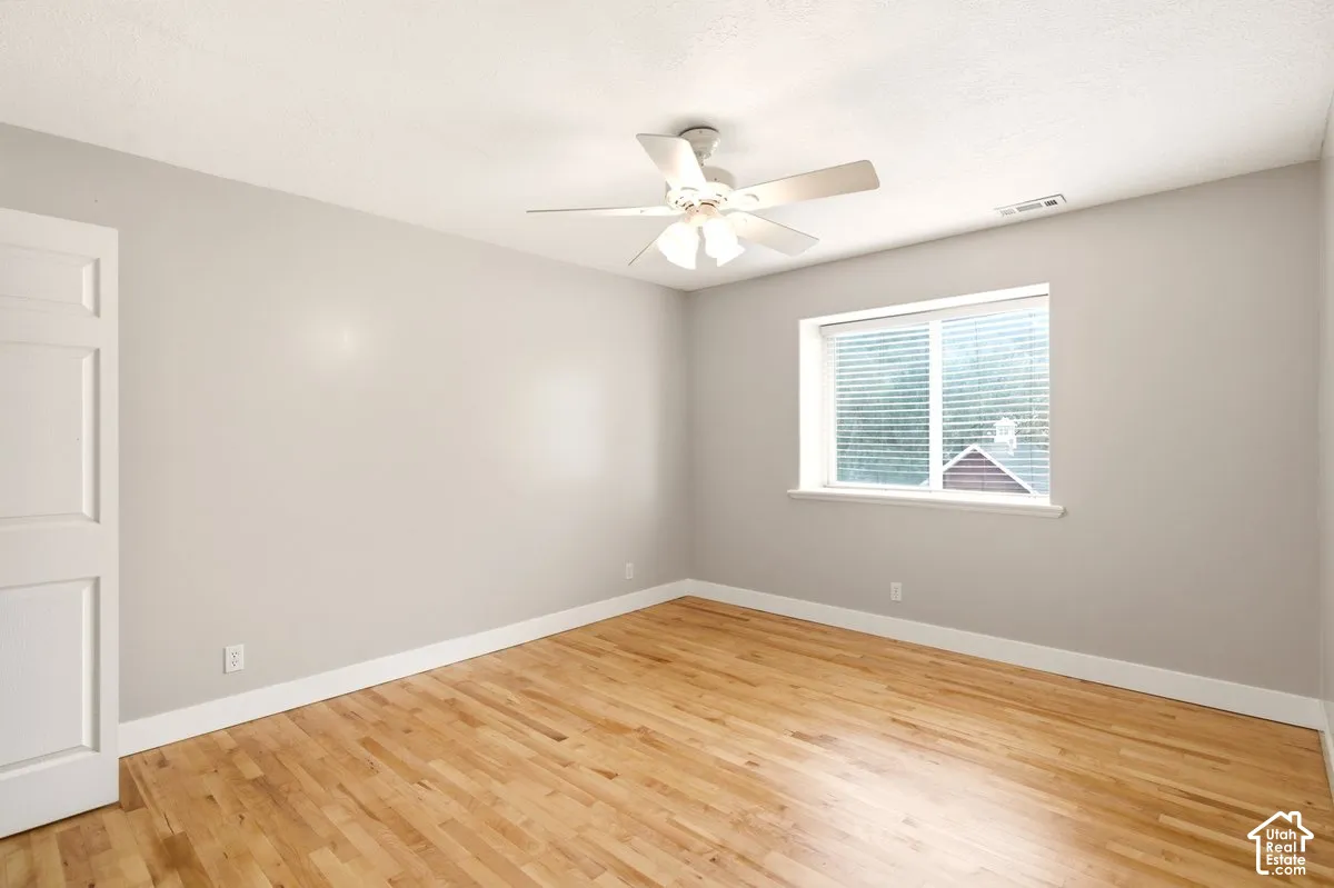 Neutral-toned walls, wood-finish flooring, ceiling fan with integrated lighting, and white multi-panel interior door