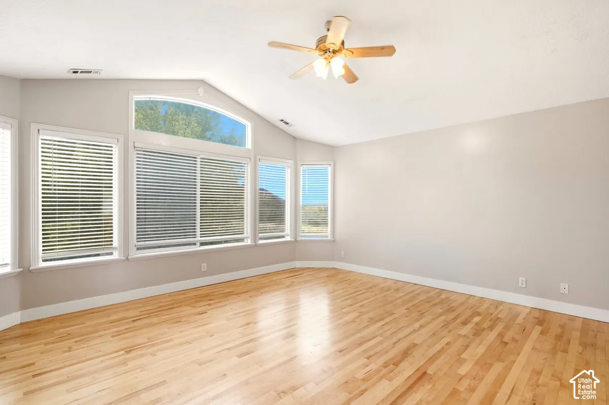 Vaulted ceiling with a centrally mounted ceiling fan, light-toned wood-finish flooring, and expansive windows featuring an arched top accent