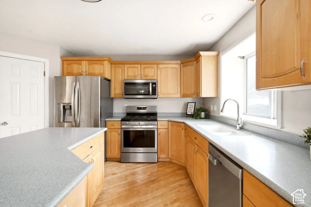 Kitchen featuring natural finish wood cabinetry, stainless steel appliances, solid-surface countertops, recessed ceiling lighting, and wood-finish flooring
