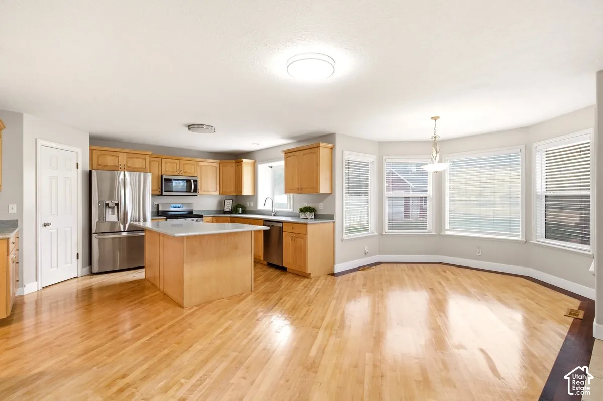 Kitchen featuring wood-finish cabinetry, an island with a countertop, stainless steel appliances, wood-finish flooring, and a bay window