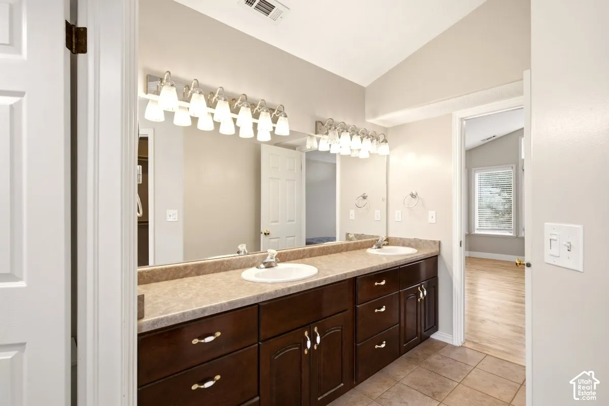 Dual-sink vanity featuring dark-finish cabinetry, solid-surface countertop with integrated backsplashes, polished metal hardware, and full-width vanity mirrors with multi-bulb light fixtures