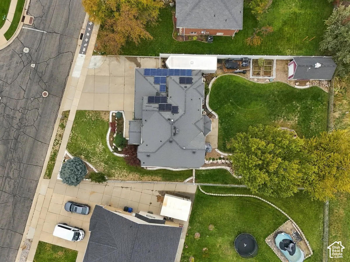 Aerial perspective of a corner lot property featuring a multi-gable roof with integrated solar panels, an expansive backyard, concrete driveway, and established landscape beds