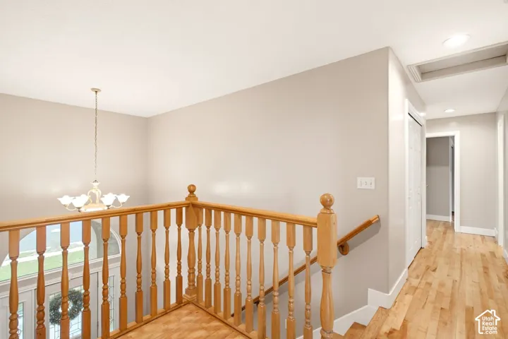 Hardwood flooring, natural wood staircase railing with turned balusters, multi-arm chandelier, and recessed lighting