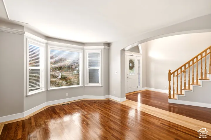Wood-finish flooring, bay window, arched entryway, and staircase with wooden handrail