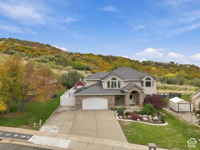 Multi-story residence featuring a stone and siding facade, arched entryway, attached multi-car garage, and landscaped front grounds against a hillside backdrop