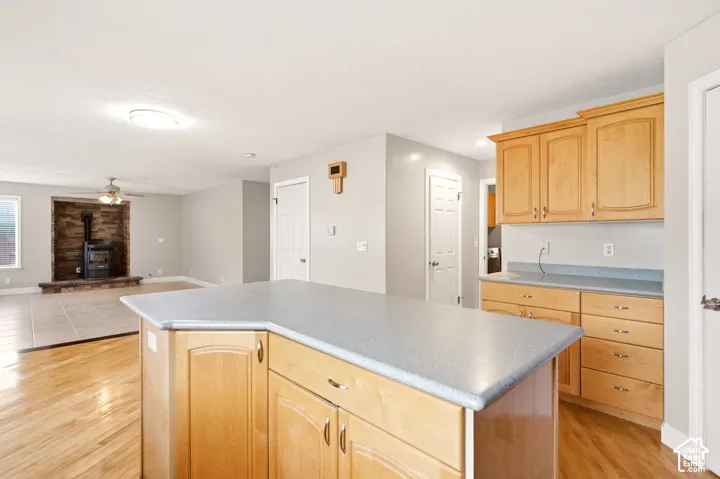 Kitchen featuring light-finish cabinetry, a central island with a laminate countertop, and wood-finish flooring, incorporating a stone-faced fireplace with a built-in insert