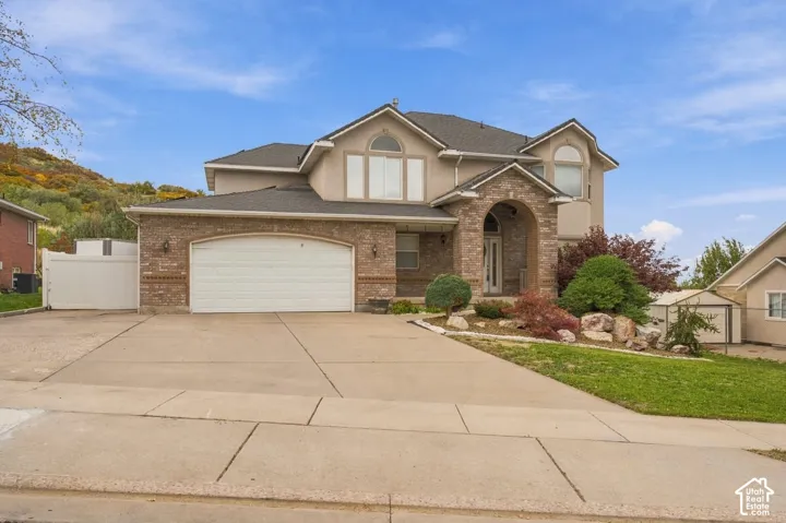 Two-story residence featuring a mixed brick and stucco exterior, arched covered entryway, multi-gabled roofline, concrete driveway, and custom-shaped windows