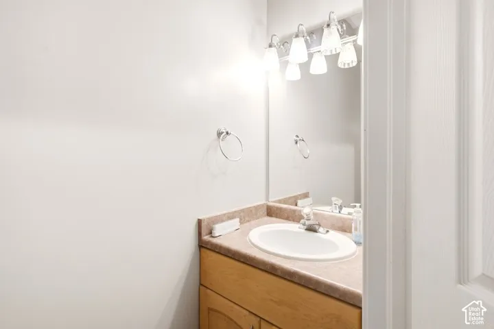 Bathroom vanity featuring wood-finish cabinetry, stone-composite countertop, oval undermount sink, wall-mounted mirror, and multi-bulb vanity lighting