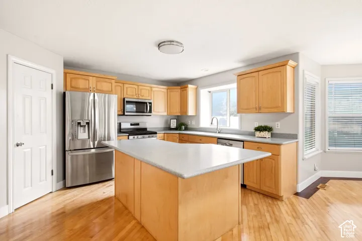 Kitchen featuring natural wood cabinetry, central island, stainless steel appliances, solid-surface countertops, and wood-finish flooring