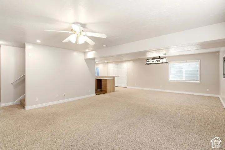 Open-concept interior featuring neutral wall tones, wall-to-wall carpeting, a multi-blade ceiling fan with integrated light fixture, recessed ceiling lighting, and built-in cabinetry with a countertop