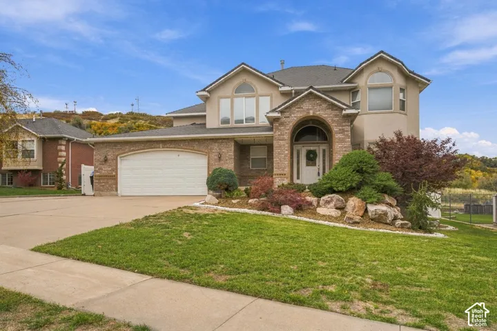 Multi-level exterior featuring a brick and stucco facade, arched entryway, multi-gabled roofline, attached multi-car garage, and landscaped rock garden