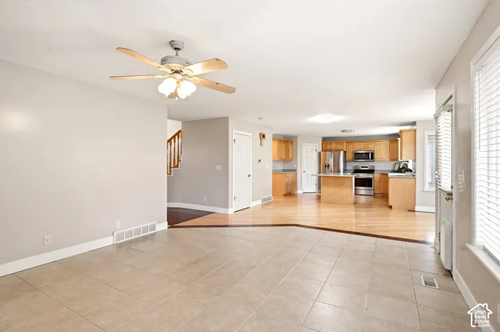 Ceramic tile flooring, wood-finish kitchen cabinetry, stainless steel appliances, kitchen island, and a ceiling fan with integrated lighting