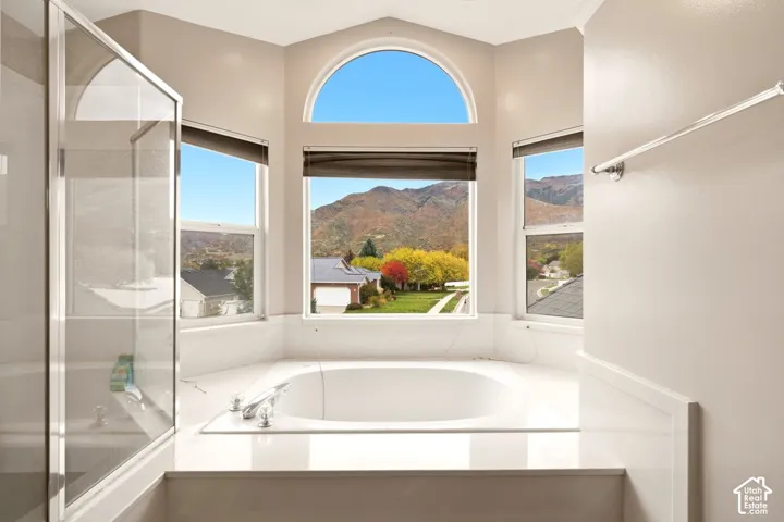 Soaking tub set in a bay window surround, arch-top picture window, and polished stone-surfaced deck with chrome faucet hardware