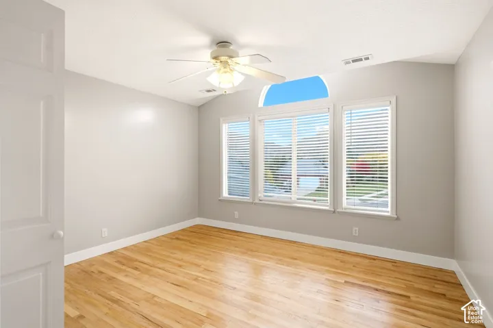 Interior room featuring wood-finish flooring, a vaulted ceiling, a centralized ceiling fan with integrated light, and three windows including an arched transom