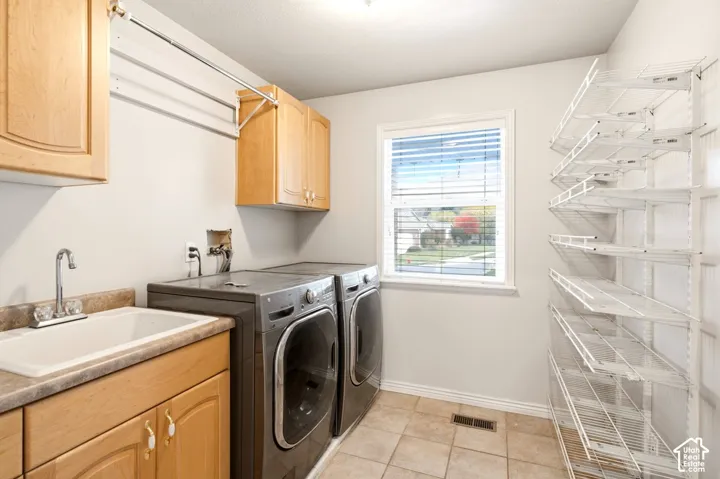 Laundry area featuring light wood-finish cabinetry, a utility sink with a stone-finish countertop, wall-mounted metal shelving, and ceramic tile flooring