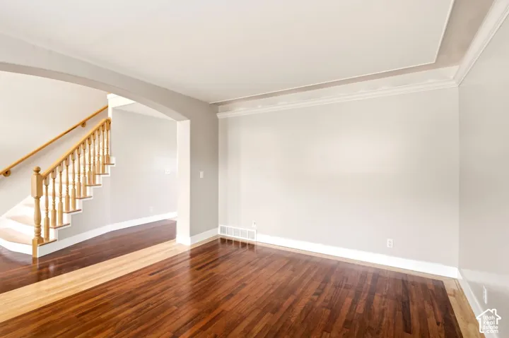 Wood-finish flooring, crown molding, and a staircase featuring a wooden handrail and balusters
