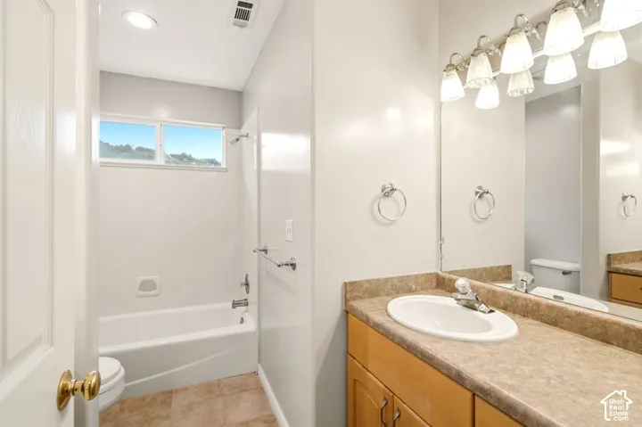 Bathroom featuring a wood-finish vanity with a stone-composite countertop, integrated sink, full-width mirror with overhead multi-light fixture, and a tub-shower combination with a tiled surround