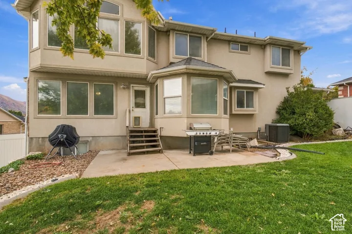 Two-story stucco exterior featuring multi-pane windows, a concrete rear patio, and a grass lawn