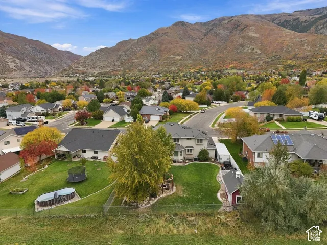 Aerial perspective of a residential property featuring a sprawling lawn, mature landscaping, and a mountainous backdrop