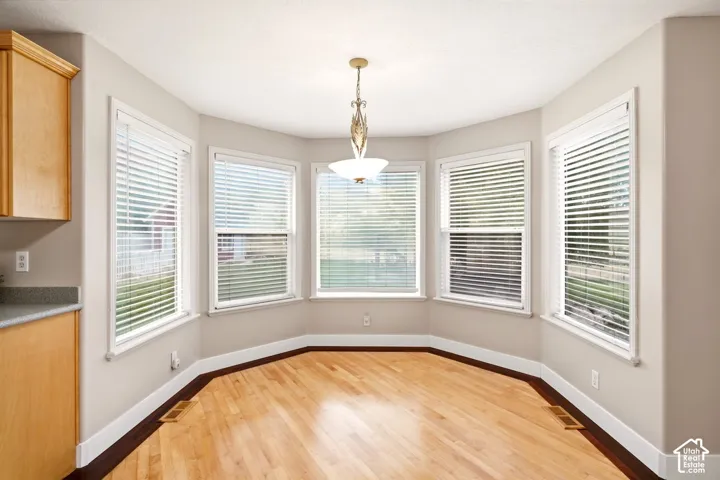 Bay window featuring wood-finish flooring, light wood cabinetry, stone-texture countertops, and a central pendant light fixture