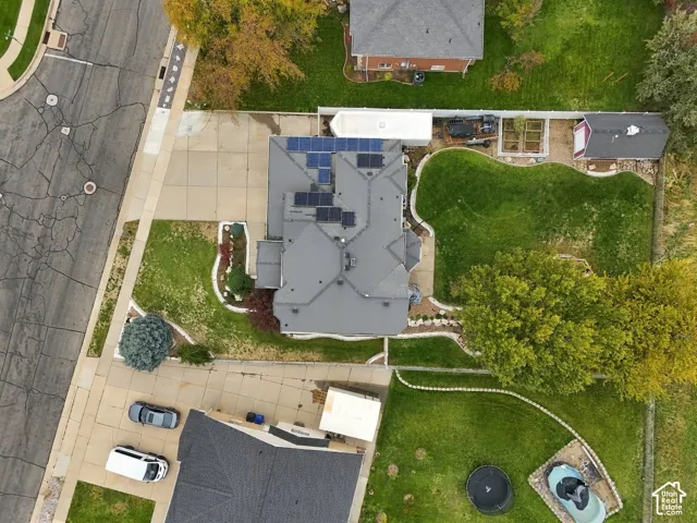 Aerial perspective of a corner lot property featuring a multi-gable roof with integrated solar panels, an expansive backyard, concrete driveway, and established landscape beds