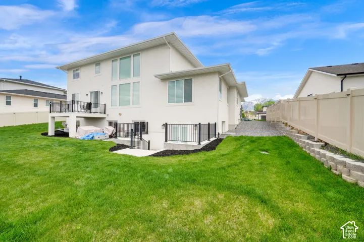 Exterior elevation featuring light-toned stucco siding, raised deck with black metal railing, stone-finished retaining wall, and fenced perimeter