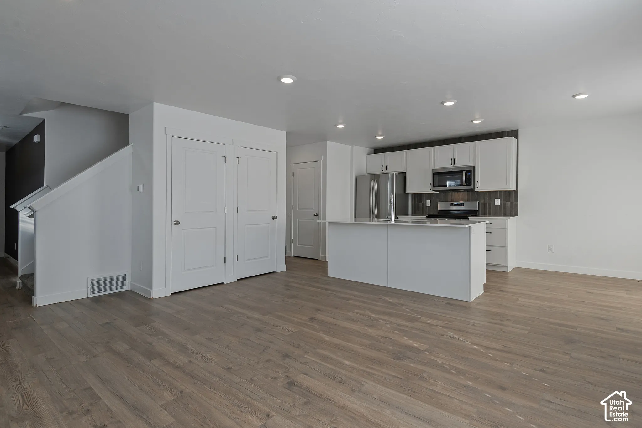 Kitchen featuring white shaker-style cabinetry, an island with countertop seating, stainless steel appliances, and wood-finish flooring