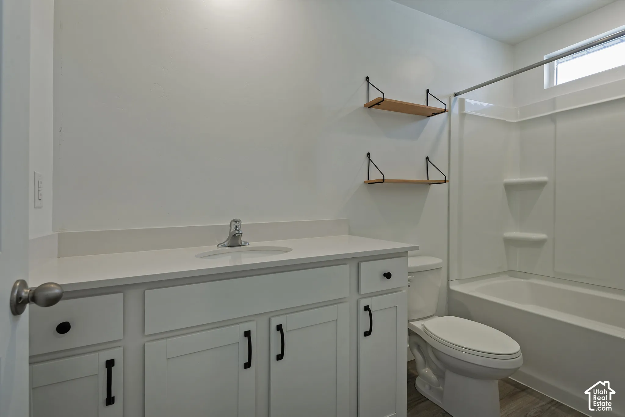 Bathroom featuring white shaker-style cabinetry with matte black hardware, quartz countertop with an integrated oval sink, built-in wooden wall shelving, and a tub-shower combination with a surround