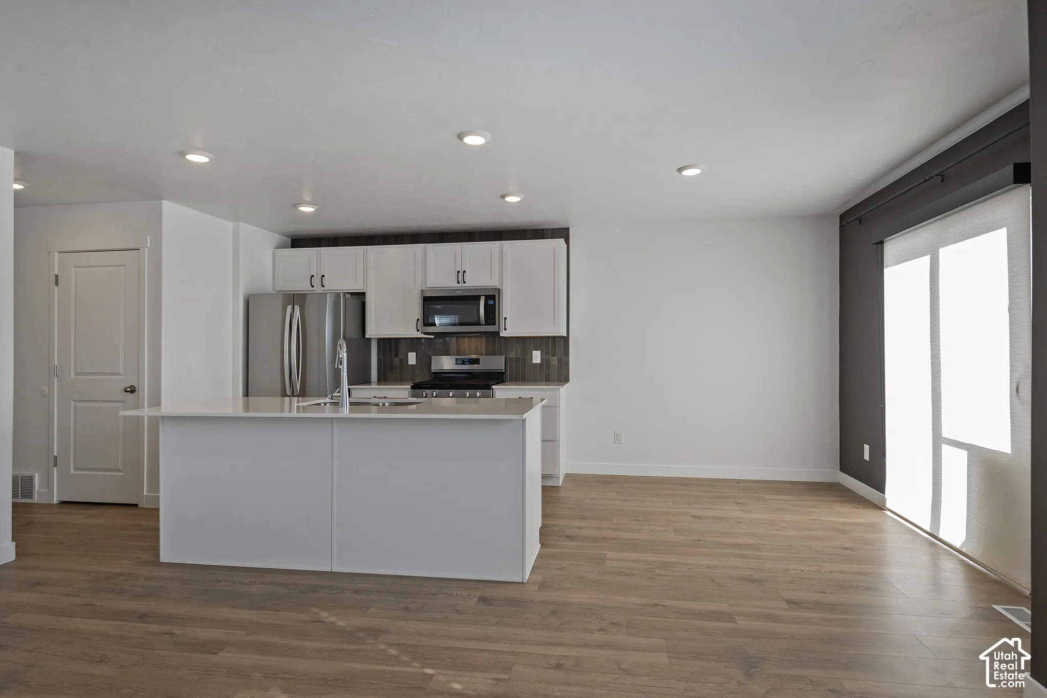 Kitchen featuring white shaker-style cabinetry, wood-finish flooring, a central island with a solid-surface countertop, stainless steel appliances, and recessed lighting